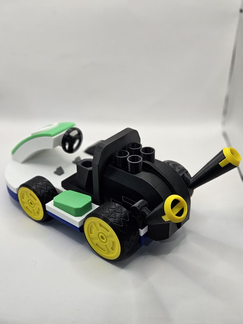 May include: A 3D-printed toy race car in black, white, green, and yellow. The car features a black body with yellow accents, a white base, and green and blue details. The wheels are yellow with black tires, and it includes a green and white remote control.