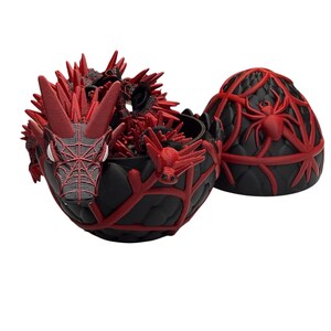 May include: A black and red dragon-themed container with a matching lid. The container is open, revealing a detailed red dragon figure inside. The lid features a spider design. The container is likely used for storage or display.