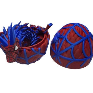 May include: A red and blue Spider-Man themed container with a lid. The container is red with blue web-like accents. The open container has a blue interior and a Spider-Man figure on the side.