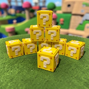 May include: A collection of yellow question mark blocks, reminiscent of a popular video game. Each block features a white question mark on all sides and small red dots. The blocks are arranged on a green surface, with a blurred background.