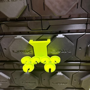 May include: A stack of black interlocking tiles with the word "LINK" embossed on each. A bright green plastic support and several matching circular pieces are placed on top, creating a contrast of colors and textures.