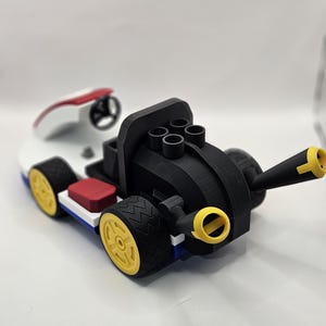 May include: A 3D-printed toy race car in a vibrant color scheme. The car features a black body with yellow wheels, a white and red cockpit, and a red seat. The design includes a steering wheel and a cannon-like element.