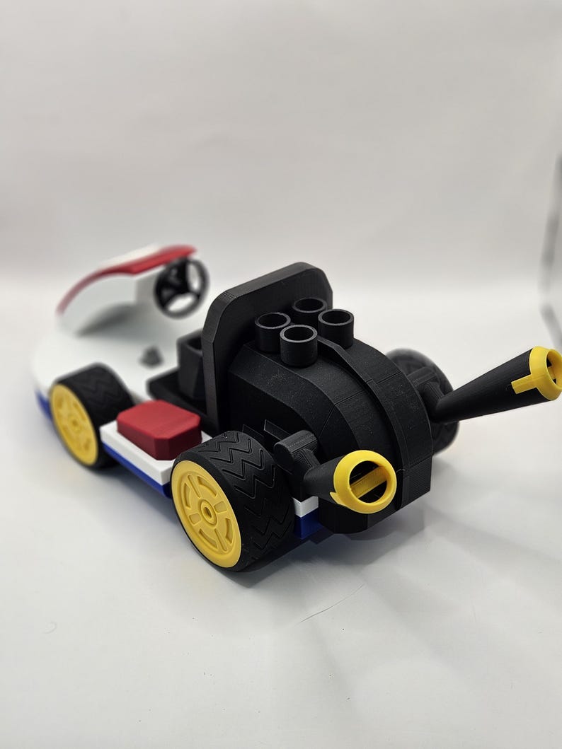 May include: A 3D-printed toy race car in a vibrant color scheme. The car features a black body with yellow wheels, a white and red cockpit, and a red seat. The design includes a steering wheel and a cannon-like element.