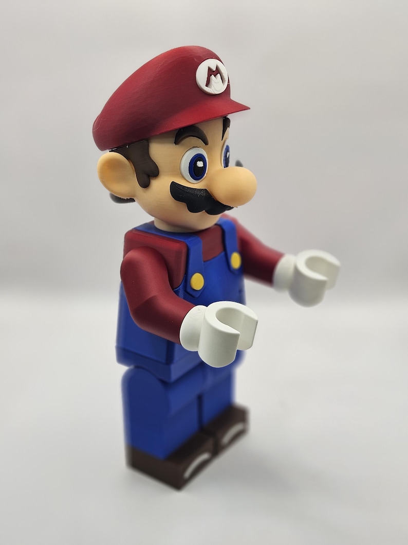 Op de afbeelding: Een beeldje van het videogamepersonage Mario. De figuur draagt een rode hoed met een witte "M" erop, een rood shirt met lange mouwen, een blauwe overall en bruine schoenen. De figuur heeft witte handen en een grote neus.