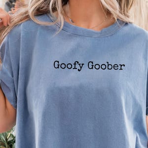 Può includere: T-shirt azzurra con la scritta nera "Goofy Goober". La maglietta ha maniche corte e una vestibilità ampia. La maglietta è realizzata in un materiale morbido.