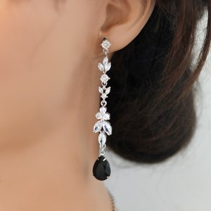 May include: Silver drop earrings with a black, teardrop-shaped stone. The earrings have a floral and leaf design with clear, sparkling accents. A matching necklace is partially visible, suggesting a jewellery set.