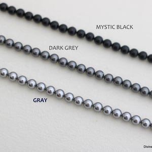 May include: Three strands of round beads arranged horizontally. The top strand is labeled MYSTIC BLACK, the middle strand is labeled DARK GREY, and the bottom strand is labeled GRAY. Each strand consists of uniform, smooth, spherical beads.