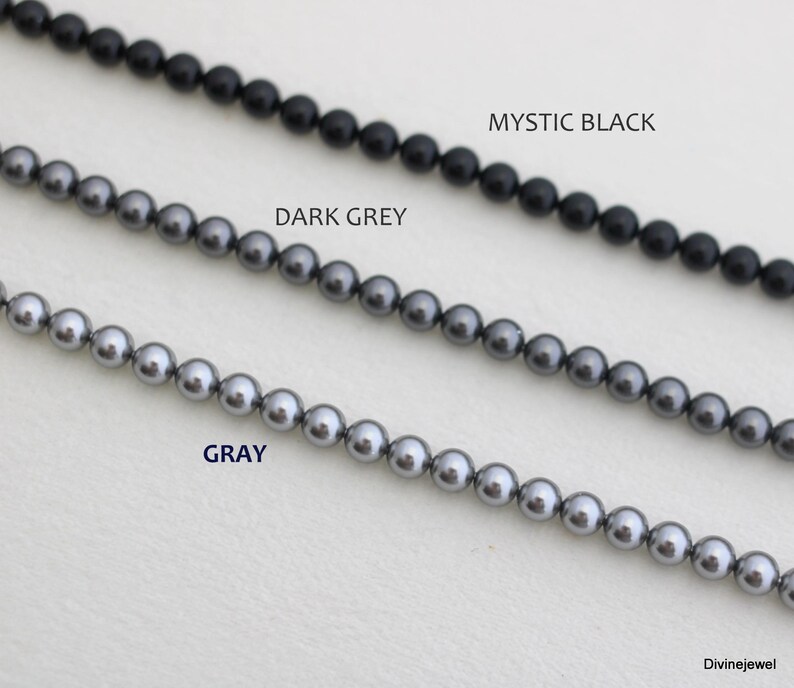 May include: Three strands of round beads arranged horizontally. The top strand is labeled MYSTIC BLACK, the middle strand is labeled DARK GREY, and the bottom strand is labeled GRAY. Each strand consists of uniform, smooth, spherical beads.