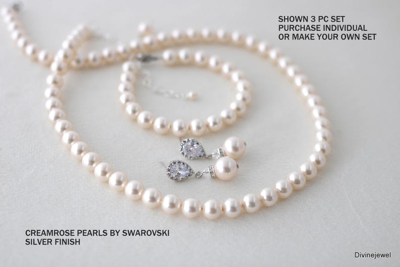 K&ouml;nnte beinhalten: Ein Schmuckset mit cremefarbenen Swarovski-Perlen und silberfarbenen Metallelementen. Das Set besteht aus einer Perlenkette, einem Armband und zwei Ohrh&auml;ngern mit einem birnenf&ouml;rmigen Kristall. Text: SHOWN 3 PC SET PURCHASE INDIVIDUAL OR MAKE YOUR OWN SET. CREAMROSE PEARLS BY SWAROVSKI SILVER FINISH. Divinejewel.
