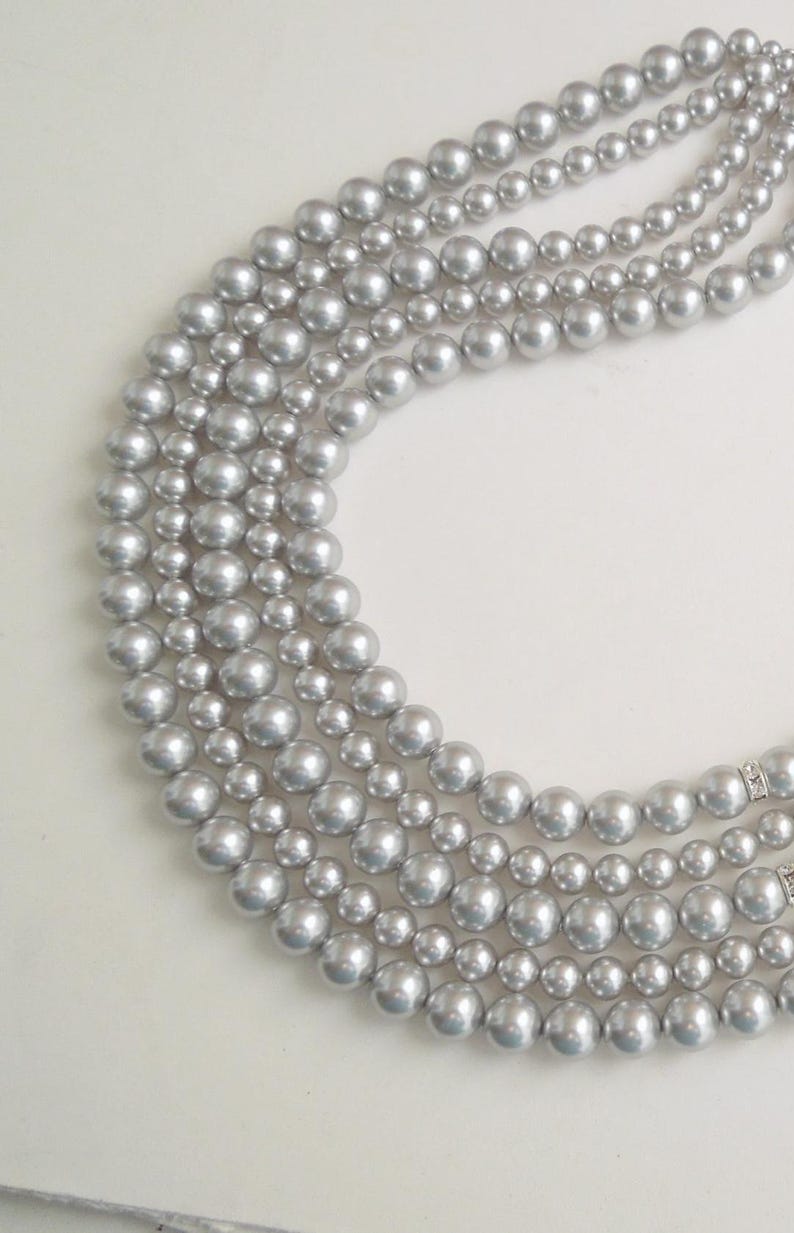 May include: A multi-strand necklace featuring four rows of round, metallic silver-toned beads. The beads are uniform in size within each strand, with the strands varying in length to create a layered effect. Small, clear crystal-encrusted spacers are visible on the strands.