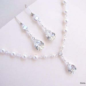K&ouml;nnte beinhalten: Ein filigranes Schmuckset mit Halskette und Ohrringen. Die Halskette hat eine Kette aus kleinen Perlen und einen tropfenf&ouml;rmigen Kristallanh&auml;nger. Die Ohrringe haben ein &auml;hnliches Design, mit einem runden Kristall und einem Tropfenkristall. Das Schmuckset ist silberfarben.