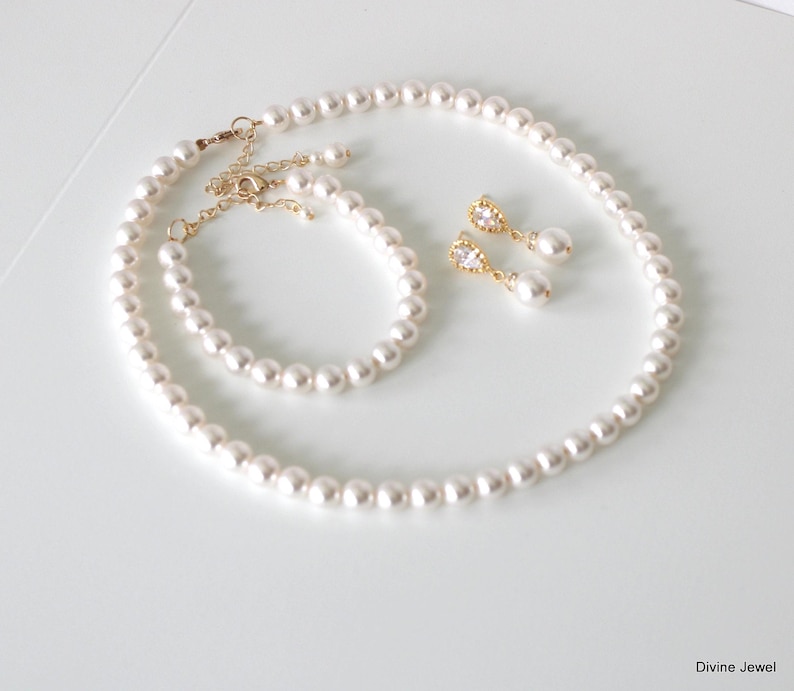 K&ouml;nnte beinhalten: Ein Schmuckset bestehend aus einer wei&szlig;en Perlenkette, einem passenden Perlenarmband mit goldenem Karabinerverschluss und Verl&auml;ngerungskette sowie zwei Ohrh&auml;ngern mit einem klaren tropfenf&ouml;rmigen Stein &uuml;ber einer einzelnen wei&szlig;en Perle.