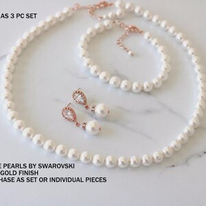 K&ouml;nnte beinhalten: Ein dreiteiliges Schmuckset mit wei&szlig;en Swarovski-Perlen und ros&eacute;goldfarbenem Finish. Das Set besteht aus einer Halskette, einem Armband und einem Paar Ohrh&auml;nger mit klaren, tropfenf&ouml;rmigen Steinen. Text: SHOWN AS 3 PC SET, WHITE PEARLS BY SWAROVSKI, ROSE GOLD FINISH, PURCHASE AS SET OR INDIVIDUAL PIECES.