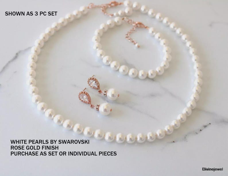 K&ouml;nnte beinhalten: Ein dreiteiliges Schmuckset mit wei&szlig;en Swarovski-Perlen und ros&eacute;goldfarbenem Finish. Das Set besteht aus einer Halskette, einem Armband und einem Paar Ohrh&auml;nger mit klaren, tropfenf&ouml;rmigen Steinen. Text: SHOWN AS 3 PC SET, WHITE PEARLS BY SWAROVSKI, ROSE GOLD FINISH, PURCHASE AS SET OR INDIVIDUAL PIECES.