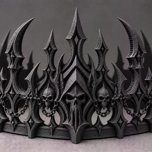 May include: A dark grey crown featuring a series of sharp, pointed spires and intricate gothic arches. The design incorporates multiple skull motifs integrated into the structure, connected by small, delicate chains that drape between the arches.