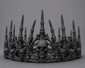 May include: A matte black crown featuring a series of human skulls integrated into the base. The structure is composed of elongated, skeletal finger-like spikes that rise vertically, creating a detailed, textured, and dark ornamental headpiece.
