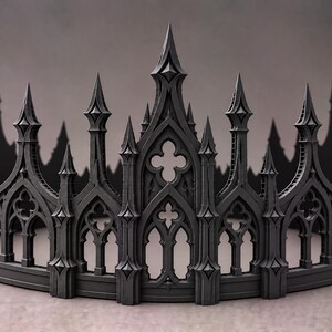 May include: A matte black crown featuring intricate architectural details reminiscent of gothic cathedral spires and pointed arches. The circular headpiece displays repeating vertical towers and open quatrefoil cutouts along the entire band.