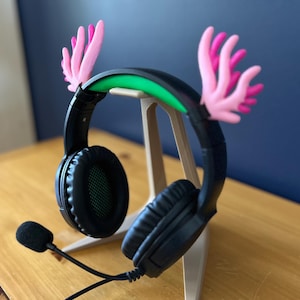 May include: Black gaming headset with a green light strip and pink antlers attached to the headband. The headset is on a stand.