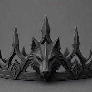 May include: A dark grey crown featuring a central geometric wolf head motif. The crown has a textured surface with sharp, pointed spikes and diamond-shaped accents containing etched symbols along the circular base band structure.