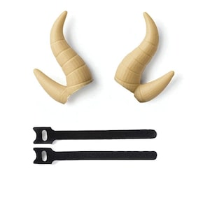 May include: Two light tan, curved horns with ridged detailing, and two black straps with a loop at one end. The horns are likely for a costume or decorative purpose, and the straps may be for attachment.