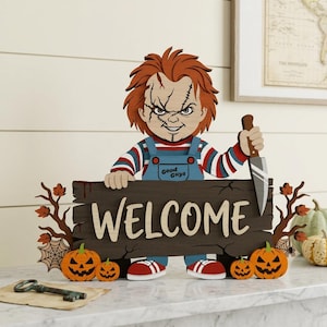 Op de afbeelding: Een decoratief houten bord met een stripfiguur met oranje haar en littekens, gekleed in een blauwe tuinbroek met de tekst Good Guys, die een zilveren mes vasthoudt. Het bord toont het woord WELCOME, geaccentueerd door oranje pompoenen en takken.