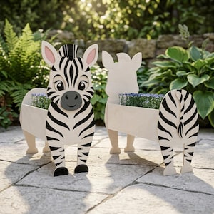 以下が含まれることがあります： 2つの木製のシマウマ型プランター。前面のシマウマは、白と黒のストライプ模様、ピンクの耳、笑顔の顔をしています。プランターボックスには小さな青い花が入っています。2番目のプランターはシマウマのシルエットです。