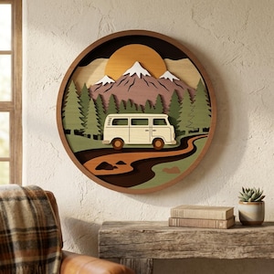 May include: A circular layered wooden wall art piece featuring a cream-coloured camper van driving on a brown road through a green pine forest. In the background, snow-capped purple mountains sit beneath a large orange sun, all framed in dark wood.