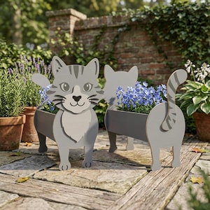 Puede incluir: Tres jardineras grises con forma de gato con flores azules. Las jardineras son de madera y tienen un diseño de dibujos animados. Las jardineras con forma de gato están en un patio de piedra con otras plantas en macetas en el fondo.