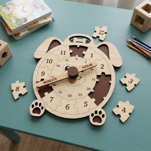 May include: A light-colored wooden puzzle clock shaped like a dog with brown accents. The clock face features numbers 1 through 12 as puzzle pieces, with a central dial showing minutes in increments of five. The hands are labeled HOUR and MINUTE.