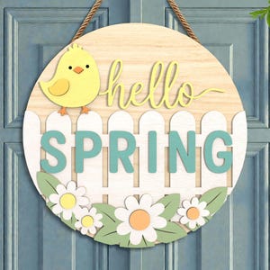 May include: A round wooden spring-themed door sign. The sign features a yellow chick, the words "hello SPRING" in light green, a white picket fence, and daisies. A brown rope is used for hanging.