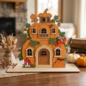 May include: A decorative wooden pumpkin house featuring two levels, arched windows, a central arched doorway, and a balcony. The structure is adorned with green leaves, red berries, small mushrooms, and acorns, all set on a flat rectangular base.
