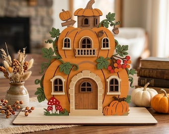 May include: A decorative wooden pumpkin house featuring two levels, arched windows, a central arched doorway, and a balcony. The structure is adorned with green leaves, red berries, small mushrooms, and acorns, all set on a flat rectangular base.