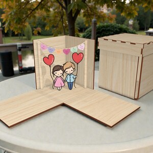 以下が含まれることがあります： 蓋付きの木箱と、L字型の開いたベース。開いた箱には、ハート型の風船を持った漫画のカップルが描かれています。ハート型のキャンディーのバナーが上にぶら下がっています。箱とベースは明るい色の木で作られています。