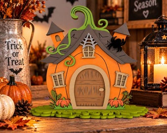 May include: A layered wooden pumpkin house decoration featuring an orange pumpkin body, a brown arched door, two side windows, a green vine stem, a grey roof with a spider web detail, and a black spider accent, all set on a green base.
