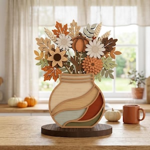 May include: A layered wooden decorative piece featuring a stylized mason jar base in shades of cream, tan, sage green, and burnt orange, filled with an arrangement of cutout flowers, wheat stalks, and autumn leaves in warm seasonal colors.
