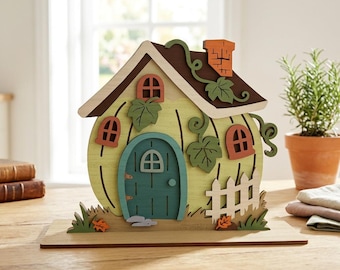 May include: A decorative wooden pumpkin-shaped house featuring a light green body with dark green vertical lines, a teal arched door, three small orange-framed windows, a brown roof, an orange chimney, and a white picket fence with green leaves.