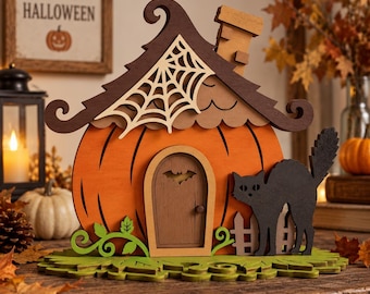May include: A decorative wooden pumpkin house featuring a dark brown roof with a cream-coloured spiderweb cutout, a central arched door with a bat silhouette, and a black cat figure standing next to a small fence on a green leaf-shaped base.