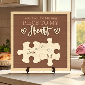 Puede incluir: Cartel enmarcado en madera con fondo marrón y marco de madera clara. El cartel dice "You Are The Missing Piece To My Heart" con dos piezas de rompecabezas. Una pieza tiene el nombre "Robin" y la otra "Will".