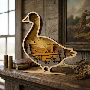 Pode incluir: Escultura de madeira em forma de pato em camadas com uma cena de caça. A obra de arte apresenta um caçador, um cão e uma paisagem com árvores e pássaros. O pato é feito de madeira castanha clara com um design interior detalhado. É exibido numa superfície de madeira.