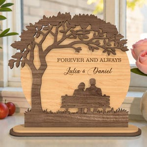 Könnte beinhalten: Ein dekoratives Holzstück mit einem Baumdesign, den Worten "FOREVER AND ALWAYS" und den Namen "Julia & Daniel". Es zeigt eine Silhouette eines Paares auf einer Bank. Das Stück ist aus hellem und dunklem Holz gefertigt.