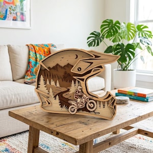 Peut inclure: Une décoration murale en bois multicouche en forme de casque de motocross. Le design présente une scène découpée au laser montrant un pilote sur une moto tout-terrain parcourant un chemin sinueux à travers une forêt avec des montagnes.
