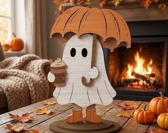 May include: A wooden cutout decoration featuring a white ghost holding a brown cup labeled Pumpkin Spice, wearing orange boots, and standing under an orange pumpkin-shaped umbrella, all mounted on a circular brown wooden base.
