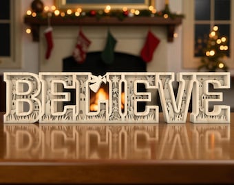 May include: A wooden, layered "BELIEVE" sign with a nativity scene design. The letters are beige and stand on a brown surface. The background includes a fireplace, Christmas stockings, and a decorated mantel.