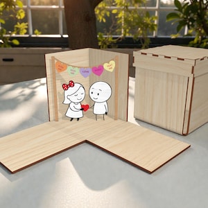 以下が含まれることがあります： 木製のポップアップカード。漫画のカップルがハートを交換しています。カードには、「HUG ME」、「LOVE」、「TEXT ME」と書かれたハート型のキャンディーのバナーが付いています。木製の箱も存在します。