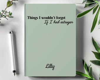 Puede incluir: Un cuaderno verde claro con el texto "Things I wouldn't forget If I had estrogen" y el nombre "Lilly" en negro. Un bolígrafo blanco está a la izquierda. Plantas verdes en el fondo.