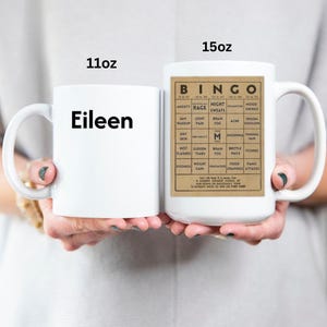 White ceramic mug featuring a vintage-style menopause bingo card design with common symptoms like brain fog, hot flashes, and mood swings. Mug shown in 11oz and 15oz sizes.  Back personalized in black.