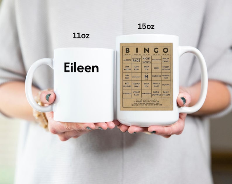 White ceramic mug featuring a vintage-style menopause bingo card design with common symptoms like brain fog, hot flashes, and mood swings. Mug shown in 11oz and 15oz sizes.  Back personalized in black.