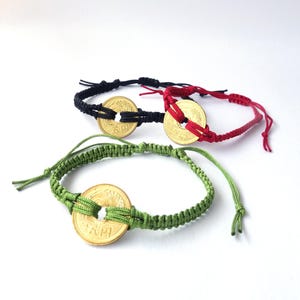 May include: Three handmade bracelets in black, red, and green. Each bracelet features a gold-colored coin as a centerpiece, with the coin's design visible. The bracelets are made of woven cord and have adjustable ties.