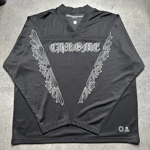 May include: A black long-sleeve V-neck jersey featuring the word CHROME in white gothic lettering across the chest. The garment includes white decorative scrollwork patterns extending from the shoulders down to the waist and a small logo at the hem.