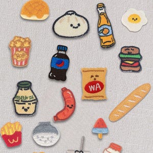 Può includere: Una collezione di toppe ricamate a tema cibo, tra cui un hamburger, pollo fritto, patatine fritte, una bottiglia di soda e un sacchetto di patatine con le lettere "WA". Altre toppe includono un raviolo, un croissant e una fetta di anguria.